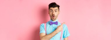 Şuna bir bak. Bıyıklı, papyonlu, hayret verici ve solu işaret eden, reklamını yapan, pembe arka planda duran beyaz bir adam..