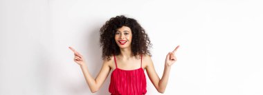 Kıvırcık saçlı, kırmızı dudaklı, gülümseyen beyaz dişli, iki tarafı gösteren, reklamları bir kenara bırakıp beyaz arka planda duran mutlu bir kadın..