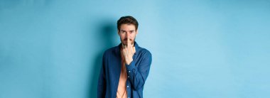 Ignorant and rude guy showing middle finger and smiling, say fuck you, standing on blue background.