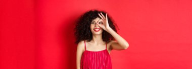 Güzel kadın heyecanla işaret ver, tanıtım teklifini kontrol et, kırmızı arka planda kırmızı renkte dur..