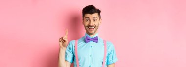 Neşeli beyaz adam bir fikir sunuyor, Eureka jestinde parmağını kaldırıyor ve gülümsüyor, çözüm öneriyor, pembe arka planda duruyor..