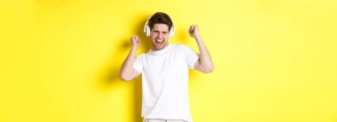 Beyaz kulaklıklarla dans eden ve müzik dinleyen mutlu bir adam, sarı arka planda duruyor. Boşluğu kopyala