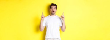 Etkilenmiş adam reklam teklifini kontrol ediyor, bakıyor ve işaret ediyor, sarı arka planda duruyor..