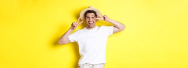 Turizm ve tatil kavramı. Mutlu turist barış işaretleriyle poz veriyor, heyecanlı gülümsüyor, sarı arka planda duruyor..