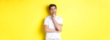 Gülümseyen bir adamın portresi sol üst köşede düşünceli görünüyor, bir şey seçiyor, bir fikri var, sarı arka planda duruyor..