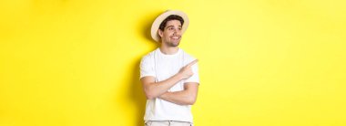 Turizm ve yaşam tarzı kavramı. Mutlu turist tanıtımı yapıyor, memnun görünüyor ve sol üst köşedeki logoyu işaret ediyor, sarı arka plan..