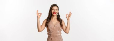 Tatmin olmuş güzel bir kadının portresi güzel bir şey öneriyor, onaylama ve gülümseme gösteriyor, kabul ya da promosyon gibi, lüks parti elbisesi içinde duruyor, beyaz arka plan.