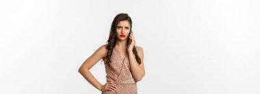 Noel partisi ve kutlama konsepti. Cazip elbiseli zarif bir kadın telefonda konuşuyor ve hoşnutsuz görünüyor, kötü haberler alıyor, beyaz arka plan.