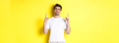 Şüpheci genç bir adam kötü bir şeyi işaret ediyor ve ona bakıyor, sarı arka planda duran bir teklifi yargılıyor..