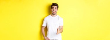 Dost canlısı bir adam seni selamlıyor, gülümsüyor, eğleniyor, merhaba diyor, sarı arka planda duruyor..