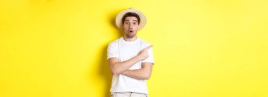 Turizm ve yaşam tarzı kavramı. Şaşkın yakışıklı turist solu işaret ediyor, reklam teklifinden etkilenmiş görünüyor, sarı arka plan.