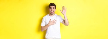 Mutlu adam söz veriyor, elini kalbe koyuyor, doğruyu söyleyeceğine yemin ediyor, sarı arka planda beyaz tişörtle dikiliyor..