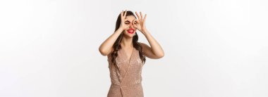 Noel partisi ve kutlama konsepti. Genç, güzel bir kadın mutlu, uzaktan bir şey görüyor, el dürbününden bakıyor, zarif bir elbise giyiyor, beyaz bir arka plan..