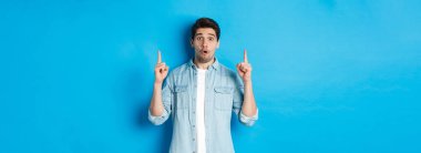 Mavi arka planda logo gösteren, parmaklarını havaya kaldıran yakışıklı bir adamın portresi..