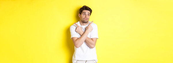 Нерешительный человек пожимает плечами, указывая пальцами в сторону, с трудом выбирает, стоя на желтом фоне.