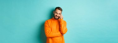 Sakallı, suratını buruşturan, utanç verici bir şeyden korkan, garip suratlı, açık mavi arka planda duran bir adam..