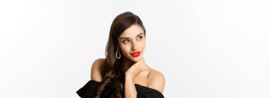 Moda ve güzellik konsepti. Küpeli, siyah elbiseli, sol şehvetli, beyaz arka planda duran zarif bir kadın. Boşluğu kopyala