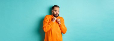 Korkak adam ürktü, korkutucu bir şeye bakıyordu, turuncu süveter içinde, stüdyo arka planında duruyordu..