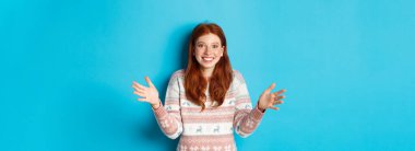 Büyük bir nesne tutan mutlu kızıl saçlı bir kız resmi. Şaşırmış görünüyor ve gülümsüyor, Noel hediyesi alıyor, mavi arka planda duruyor..