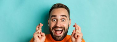 Umut dolu sakallı bir adamın dilek tutarken, şans dilemek ve parmaklarını çaprazlamak için açık mavi arka planda durduğu bir vesikalık..