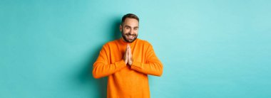 Mutlu adam teşekkür ediyor, el ele tutuşup dua ediyor, minnettar görünüyor ve gülümsüyor, açık mavi arka planda duruyor..