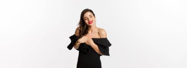 Moda ve güzellik. Şehvetli genç bir kadın mutlu görünüyor, gözleri kapalı ve nostaljik duygularla el ele tutuşuyor, beyaz arka planda duruyor..