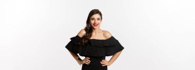 Kırmızı rujlu, siyah elbiseli, gülümseyen, beyaz arka planda duran güzel bir kadının belden yukarı pozu..