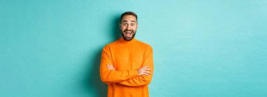 Mutlu ve şaşırmış bir adamın görüntüsü. Turkuaz arka planda turuncu süveter giymiş, hayrete düşmüş görünüyor..