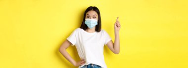 Covid, sağlık ve salgın hastalık konsepti. Tıbbi maskeli Asyalı kadın manken ve beyaz tişört sol üst köşedeki logoyu işaret ediyor..