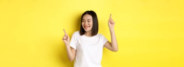 Mutlu Asyalı kadın dans ediyor ve eğleniyor, sarı arka planda beyaz tişörtle poz veriyor..