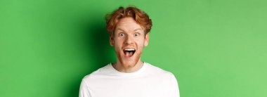 Duygular ve moda konsepti. Şaşırmış kızıl saçlı adama yakın çekim yapmak için kameraya neşeli bir şekilde bakan yeşil arka planda duran harika bir haber var..