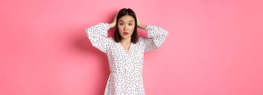 Şaşırmış ve sorunlu Asyalı kadın kafası karışmış görünüyor, el ele tutuşuyor, sorun yaşıyor, pembe arka planda duruyor..