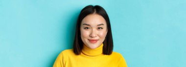 Güzellik ve cilt bakımı. Mükemmel yüzlü, kusursuz, kameraya gülümseyen, mavi arka planda duran güzel Asyalı genç kadına yakın durun..