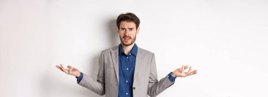 Ne olmuş yani? Kafası karışmış ve rahatsız olmuş işadamı ellerini yana açmış ve kaşlarını çatmış, anlayamamış, beyaz arka planda duruyor..