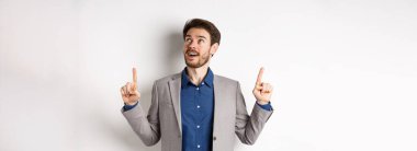 Heyecanlı, sakallı, takım elbiseli, neşeli görünüşlü, hayranlıkla tepede duran, beyaz arka planda duran yakışıklı adam..