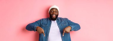 Afallamış ve etkilenmiş Afro-Amerikan bir adam reklamını yapıyor, kameraya bakıyor mutlu ve parmakları aşağıda, pembe arka planda..
