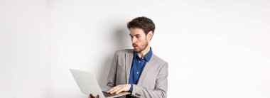 Heyecanlı satıcı dizüstü bilgisayar ekranına bakıyor şaşkın, heyecandan uzak duruyor, ağdaki haberleri kontrol ediyor, beyaz arka planda duruyor..