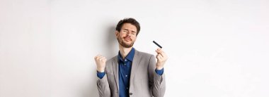 Heyecanlı başarılı iş adamı, plastik kredi kartıyla dans ediyor, yumruk tokuşturuyor ve gülümsüyor..