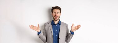 Heyecanlı takım elbiseli yönetici mutlu ve eğlenceli görünüyor. Beyaz arka planda sizi karşılamak veya tebrik etmek için ellerini yana açıyor..