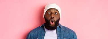 Etkilenmiş siyah erkek modelin yakın çekimi hayret içinde kameraya bakıyor ve pembe arka planda dikiliyor. Boşluğu kopyala