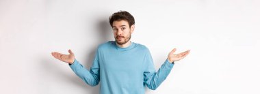 Mavi gömlekli, omuzlarını silkmiş, kameraya bakmayan, hiçbir şey bilmeyen, beyaz arka planda duran sakalsız bir adam..