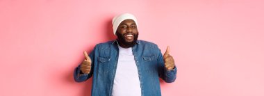 Tatmin olmuş yakışıklı siyah adam mutlu görünüyor, başparmak işareti yapıyor ve gülümsüyor, onaylıyor ve övüyor, tavsiye ediyor, pembe arka plan.
