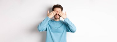 Gülümseyen beyaz adam sürpriz bekliyor, gözleri kapalı, hediye bekliyor, beyaz arka planda duruyor. Kutlama ve tatil kavramı.