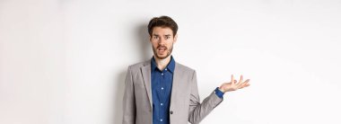 Yanlış olan ne? Takım elbiseli kafası karışık adam anlayamaz. Elleri havada, kameraya bakıyor, sorgulanıyor, beyaz arka planda duruyor..