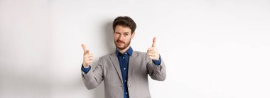 Sen halledersin. Beyaz takım elbiseli yakışıklı beyaz iş adamı kamerayı işaret ediyor ve göz kırpıyor, insanları motive ediyor, şirkette çalışmaya davet ediyor, beyaz arka planda duruyor..