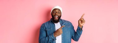 Harika bir tanıtım teklifi sunan siyahi adam, kameraya bakıyor, heyecanlı ve gülümsüyor, sol üst köşedeki afişi işaret ediyor, pembe arka plan..