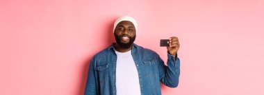 Alışveriş konsepti. Bereli memnun genç sakallı adam. Kredi kartı gösteriyor. Gülümsüyor..