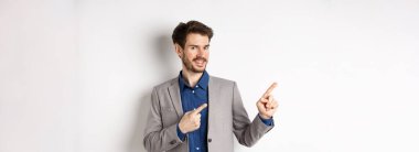 Gri takım elbiseli yakışıklı iş adamı logoyu işaret ediyor, reklamlara davet ediyor, beyaz arka planda duruyor..