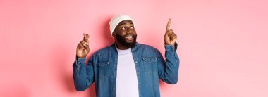 Umut dolu Afro-Amerikalı bir adam bir dilek diliyor, şans dilemek için dua ediyor, sol üst köşeyi işaret ediyor ve bakıyor, pembe bir arka plan almayı hayal ediyor..