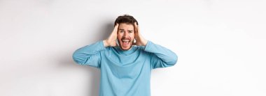 Beyaz arka planda duran, hayal kırıklığına uğramış ve bağıran, panik içinde çığlık atan genç beyaz bir adamın görüntüsü..